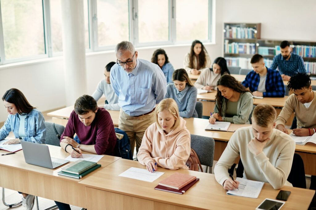 Mature professor and college students during exam in the classroom.