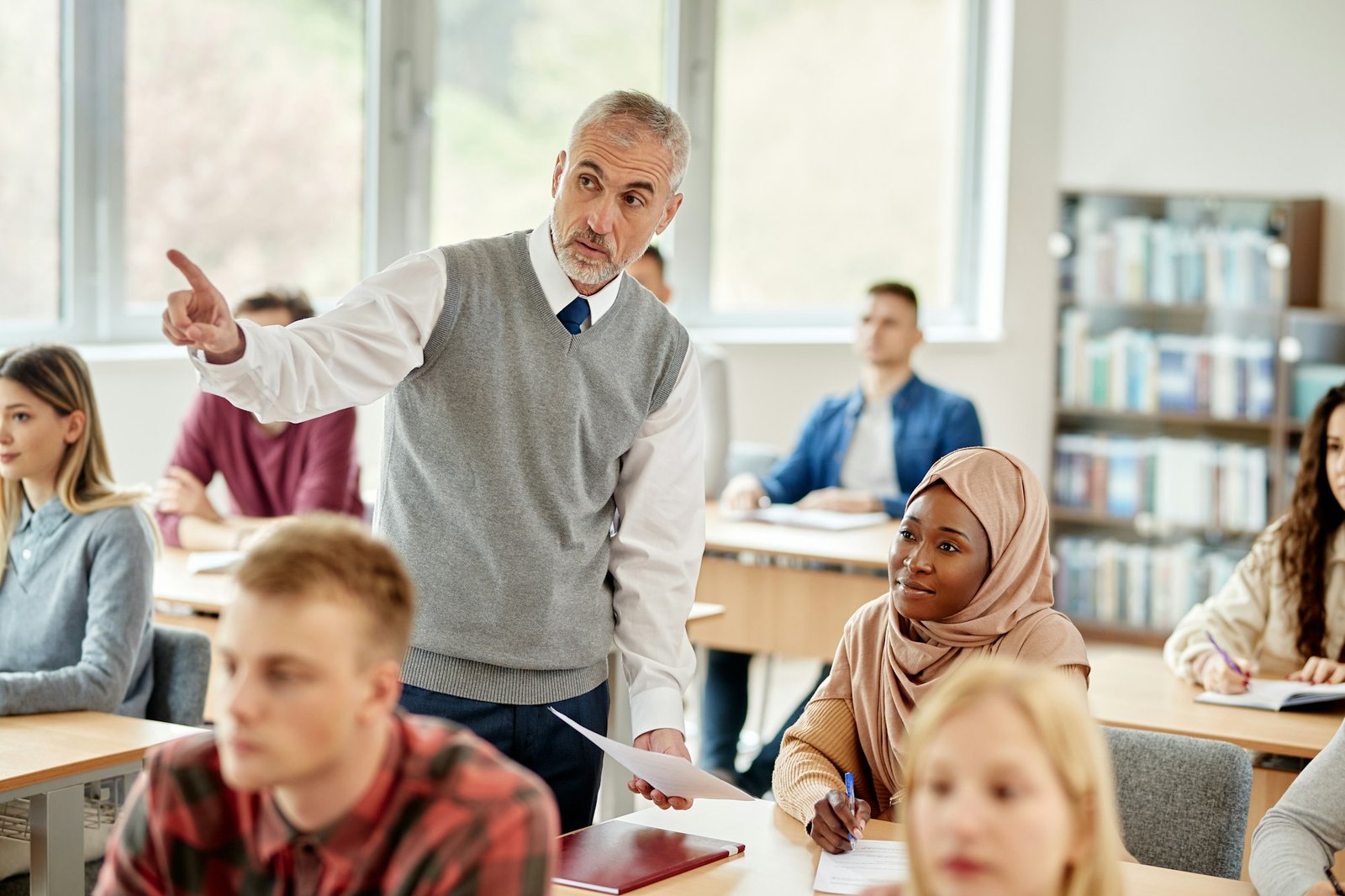 Mature teacher assisting black Islamic student during a lecture in the classroom.